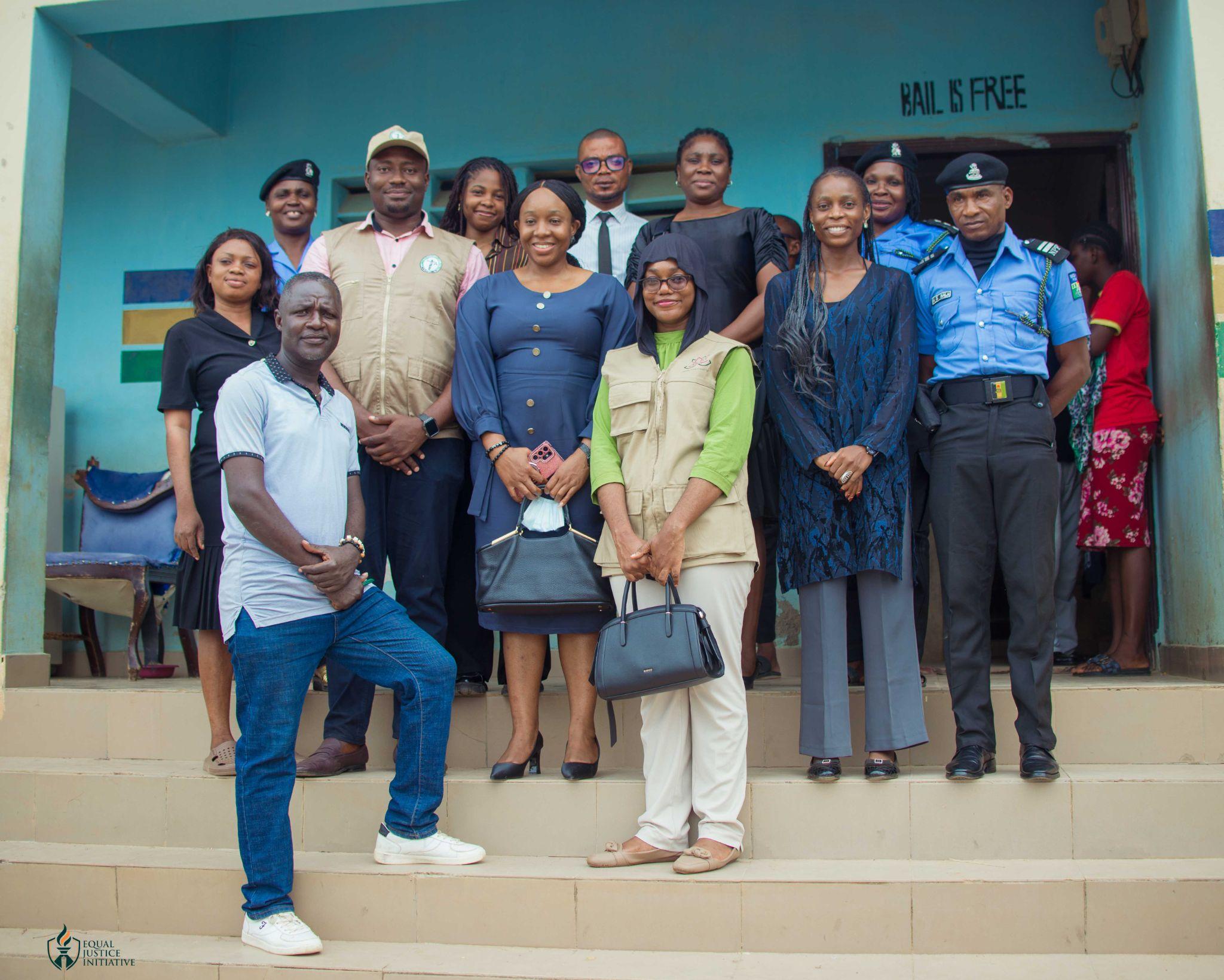 Oversight team with police officers on the steps of Ushafa Police Division, beneath a sign reading "Bail is free"